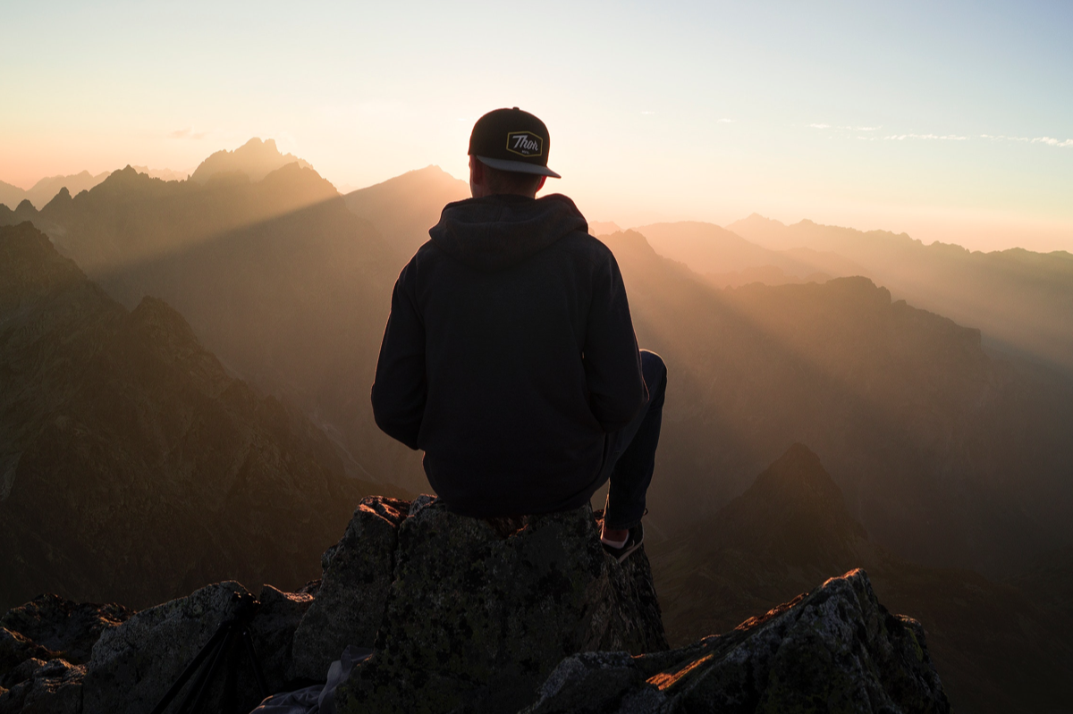 Jeune de dos sur un rocher regardant un coucher de soleil